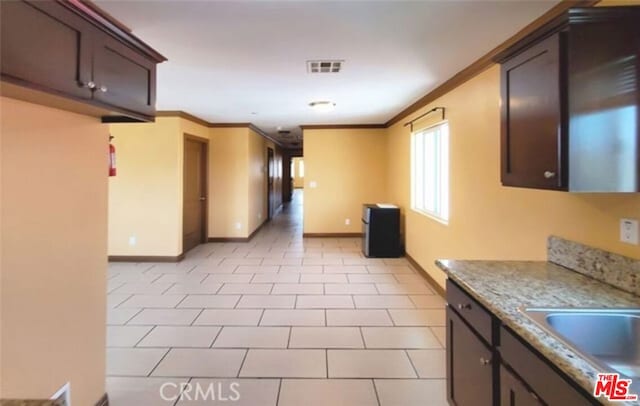 kitchen featuring ornamental molding, dark brown cabinets, light tile patterned floors, and light stone counters