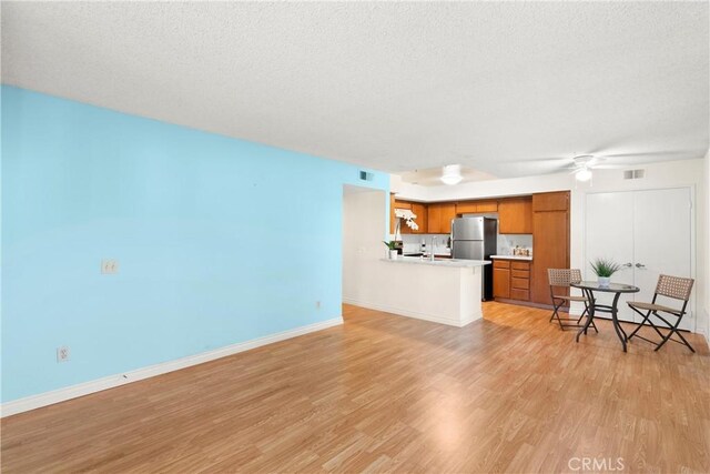 living room with ceiling fan, light hardwood / wood-style flooring, and a textured ceiling