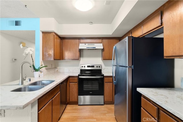 kitchen with sink, appliances with stainless steel finishes, kitchen peninsula, light stone countertops, and light hardwood / wood-style floors