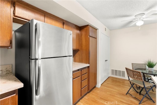 kitchen featuring stainless steel refrigerator, ceiling fan, light hardwood / wood-style flooring, and a textured ceiling