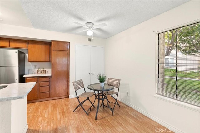 unfurnished dining area with ceiling fan, light hardwood / wood-style floors, and a textured ceiling