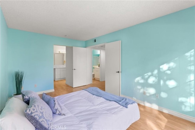 bedroom with ensuite bath, a textured ceiling, and light wood-type flooring