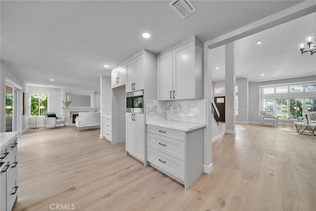 kitchen with white cabinetry, light stone counters, light hardwood / wood-style flooring, and decorative backsplash