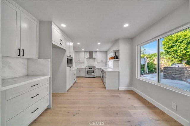 kitchen with appliances with stainless steel finishes, tasteful backsplash, sink, white cabinets, and wall chimney range hood