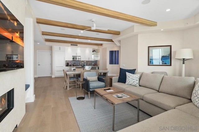 living room with ceiling fan, beam ceiling, and light hardwood / wood-style floors