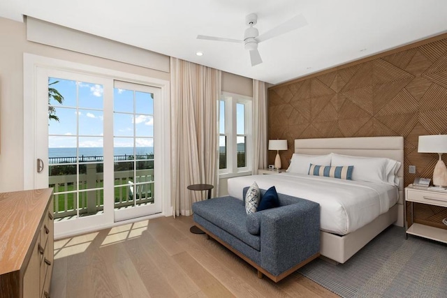 bedroom featuring ceiling fan, a water view, access to outside, and light hardwood / wood-style floors