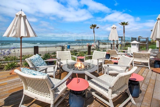 view of patio / terrace featuring a deck with water view, a beach view, and an outdoor fire pit