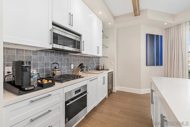 kitchen featuring sink, white cabinetry, stainless steel appliances, light hardwood / wood-style floors, and decorative backsplash