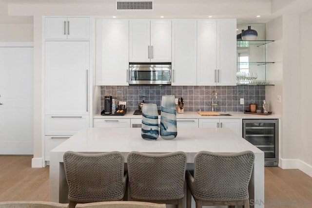 kitchen with sink, white cabinetry, tasteful backsplash, beverage cooler, and light wood-type flooring