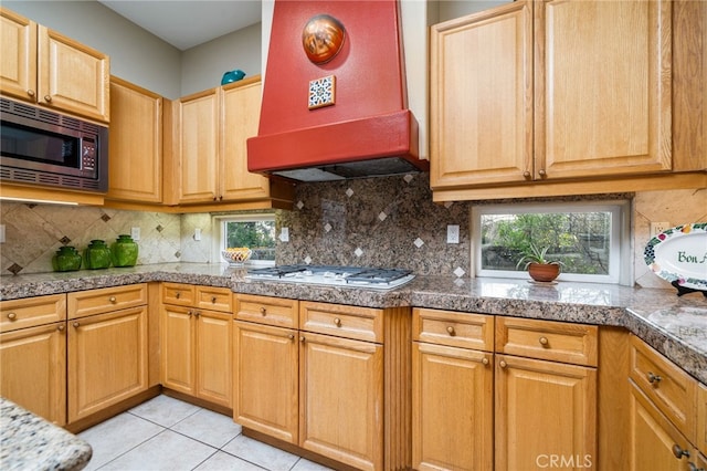 kitchen featuring stainless steel microwave, wall chimney exhaust hood, plenty of natural light, and backsplash