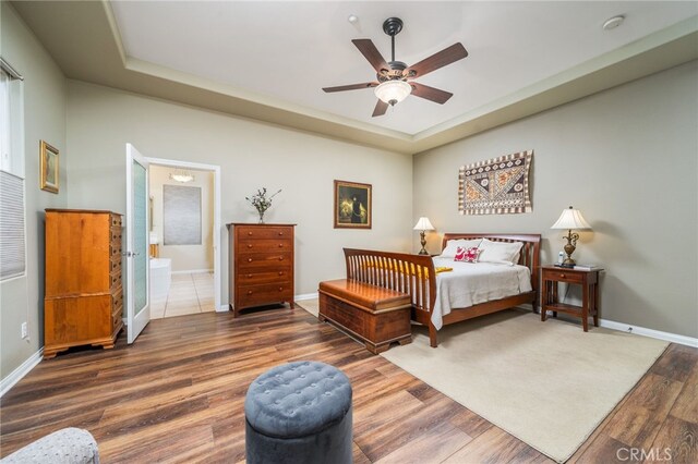 bedroom featuring dark wood-type flooring, ensuite bath, a raised ceiling, and ceiling fan