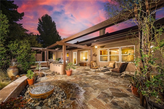 back house at dusk featuring a pergola, a patio area, and exterior kitchen