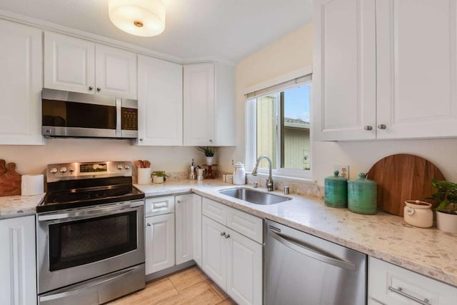 kitchen with light stone counters, appliances with stainless steel finishes, sink, and white cabinets