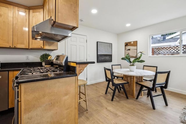 kitchen with a breakfast bar area, ventilation hood, light hardwood / wood-style flooring, stainless steel range with gas stovetop, and dark stone counters