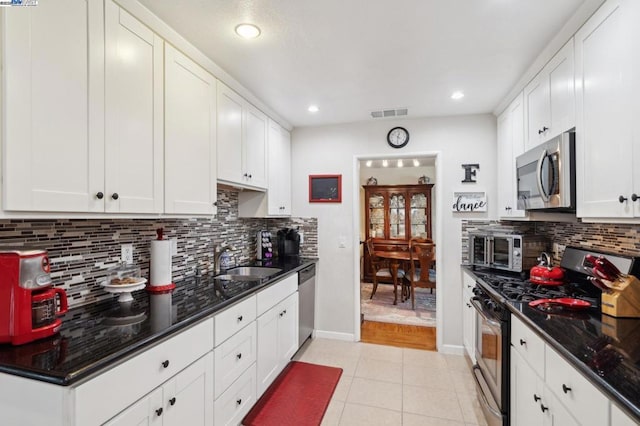 kitchen with sink, dark stone countertops, white cabinets, light tile patterned floors, and stainless steel appliances