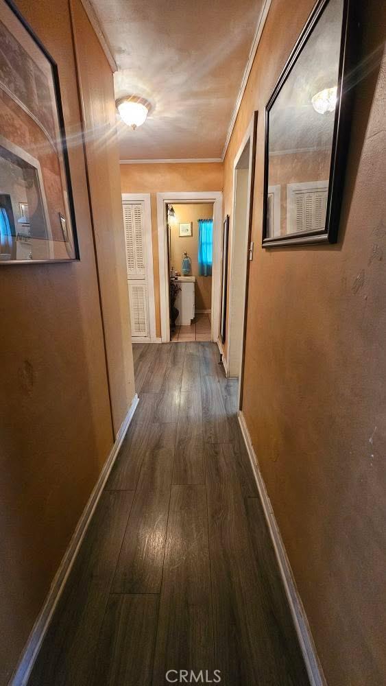 hallway featuring crown molding, baseboards, and dark wood-type flooring