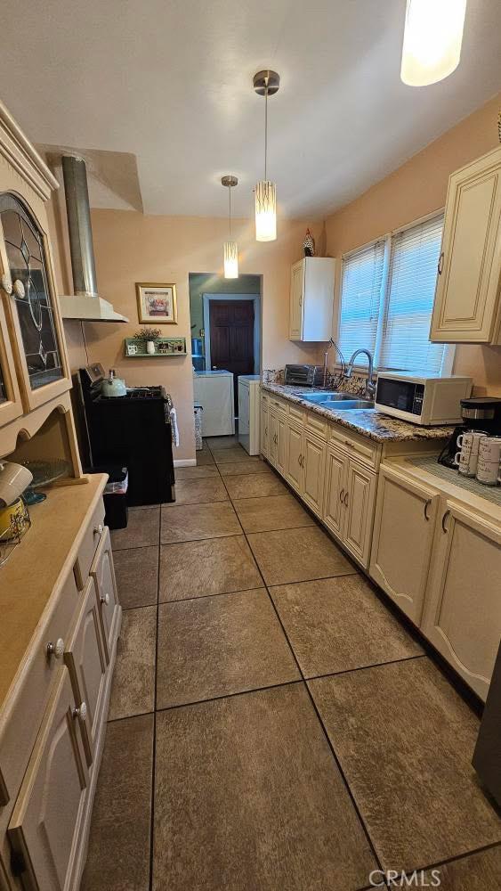 kitchen featuring cream cabinetry, white microwave, hanging light fixtures, and separate washer and dryer