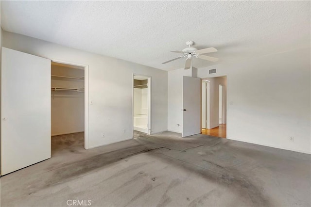 unfurnished bedroom with connected bathroom, a walk in closet, a textured ceiling, a closet, and ceiling fan