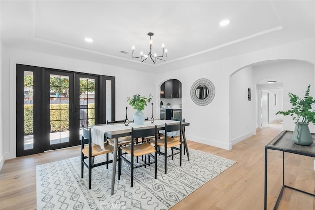 dining space with a notable chandelier, light hardwood / wood-style floors, a raised ceiling, and french doors