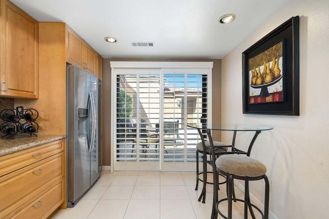 kitchen with light stone counters, light tile patterned flooring, and stainless steel refrigerator with ice dispenser