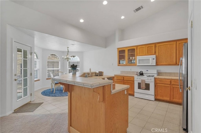 kitchen with a kitchen bar, an inviting chandelier, hanging light fixtures, tile counters, and white appliances