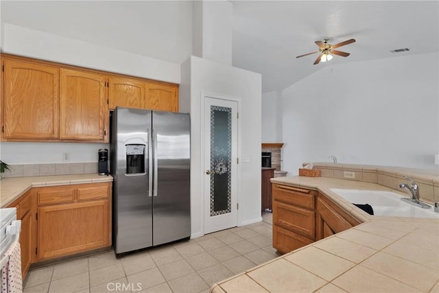 kitchen featuring sink, stainless steel fridge with ice dispenser, light tile patterned floors, tile counters, and ceiling fan