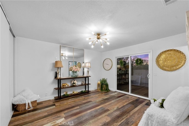 living room featuring an inviting chandelier, dark wood-type flooring, and a textured ceiling