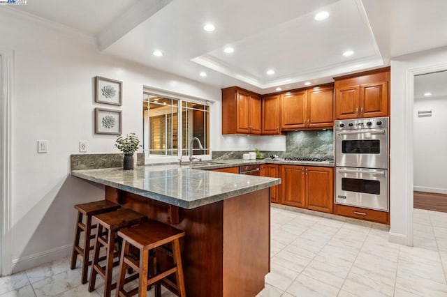 kitchen with a breakfast bar, double oven, sink, decorative backsplash, and a tray ceiling