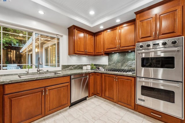 kitchen featuring sink, stainless steel appliances, stone countertops, decorative backsplash, and a raised ceiling