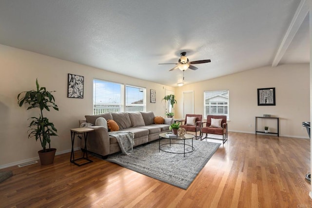 living room with a wealth of natural light, vaulted ceiling with beams, hardwood / wood-style floors, and ceiling fan