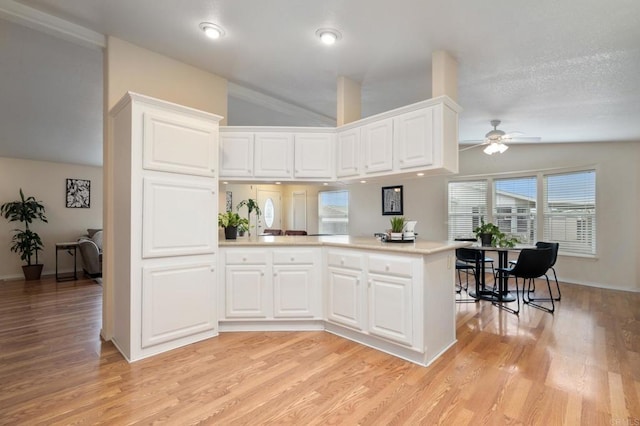 kitchen featuring lofted ceiling, white cabinets, light hardwood / wood-style floors, and kitchen peninsula