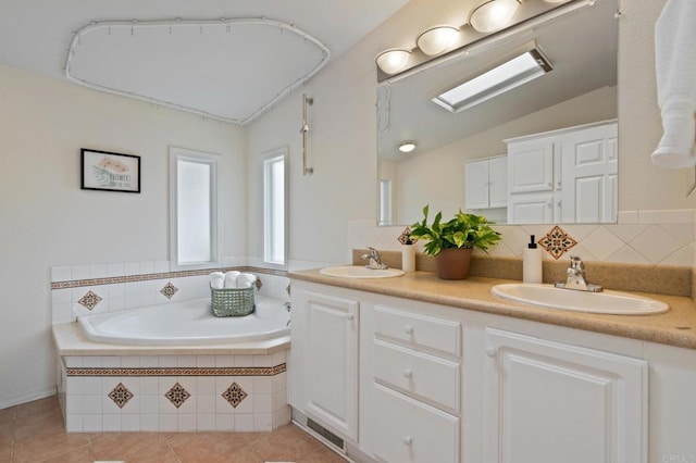 bathroom with tiled tub, backsplash, vaulted ceiling with skylight, vanity, and tile patterned floors