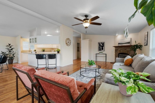 living room featuring ceiling fan, a fireplace, and light wood-type flooring