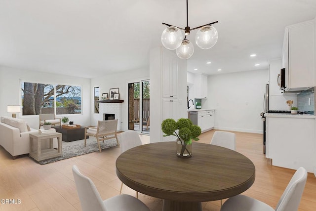 dining room featuring a brick fireplace, sink, and light hardwood / wood-style flooring