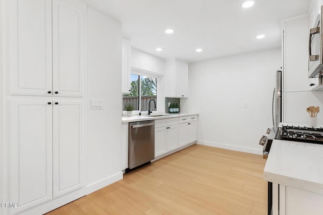 kitchen featuring stainless steel appliances, white cabinetry, sink, and light hardwood / wood-style floors