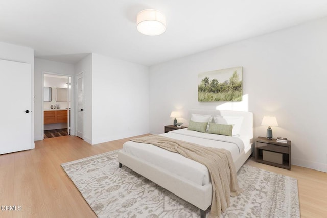 bedroom with ensuite bathroom, light wood-type flooring, and a closet