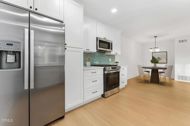 kitchen featuring light hardwood / wood-style flooring, appliances with stainless steel finishes, pendant lighting, decorative backsplash, and white cabinets