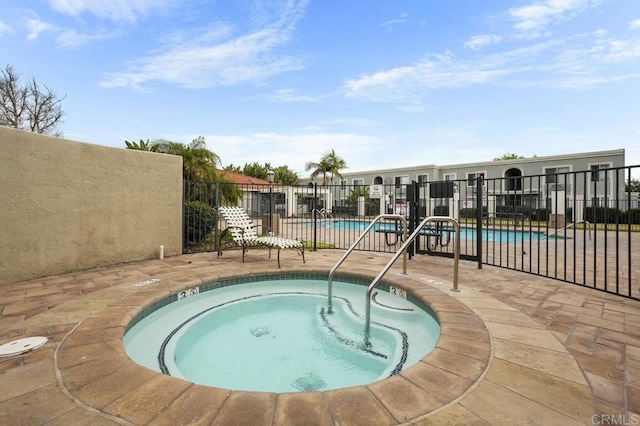 community pool featuring a hot tub, fence, and a patio