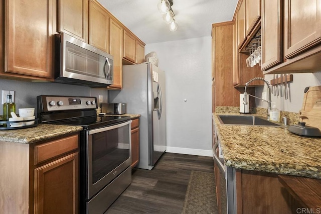 kitchen with stainless steel appliances, dark wood-type flooring, a sink, baseboards, and brown cabinetry