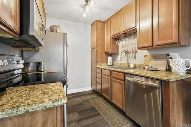 kitchen with a sink, baseboards, appliances with stainless steel finishes, brown cabinets, and dark wood finished floors