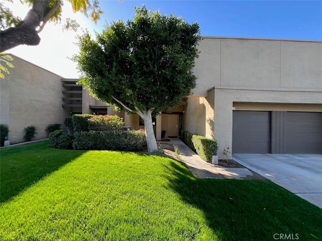 view of front of property with an attached garage, a front yard, concrete driveway, and stucco siding