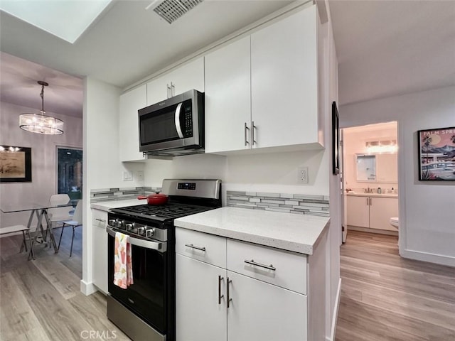 kitchen featuring visible vents, light wood-style flooring, appliances with stainless steel finishes, white cabinetry, and pendant lighting