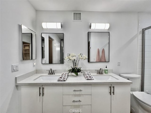 bathroom featuring toilet, double vanity, a sink, and visible vents