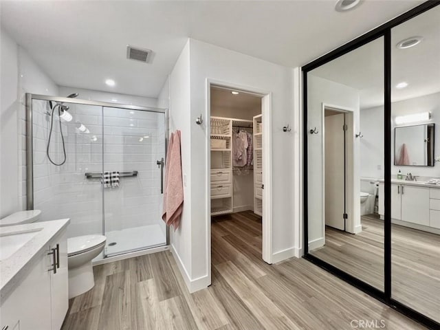 bathroom featuring toilet, wood finished floors, vanity, a stall shower, and a walk in closet