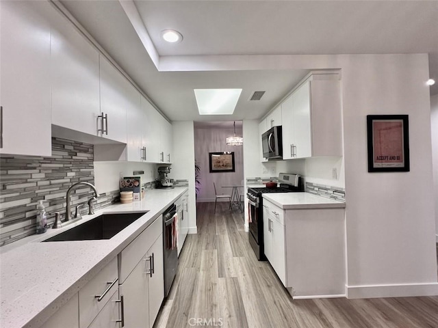 kitchen featuring tasteful backsplash, white cabinets, appliances with stainless steel finishes, hanging light fixtures, and a sink