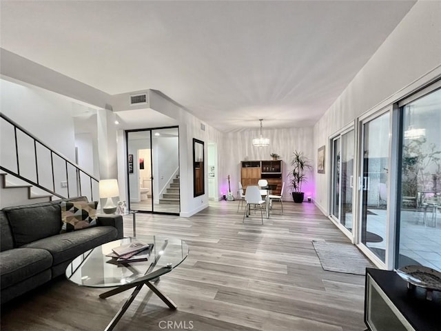 living room featuring visible vents, an inviting chandelier, light wood-type flooring, baseboards, and stairs