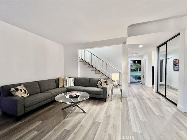 living room with stairs, light wood-type flooring, and baseboards