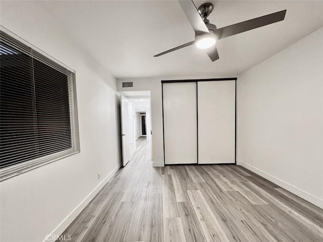 unfurnished bedroom featuring visible vents, baseboards, a ceiling fan, light wood-style flooring, and a closet