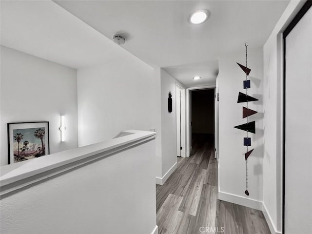 hall featuring light wood-style floors, recessed lighting, baseboards, and an upstairs landing