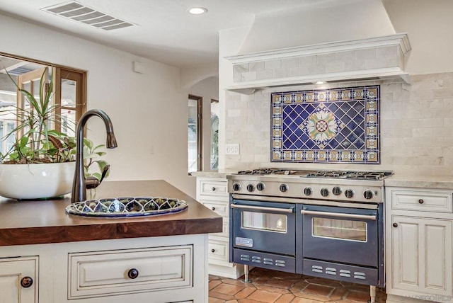 kitchen with white cabinetry, sink, backsplash, range with two ovens, and custom range hood